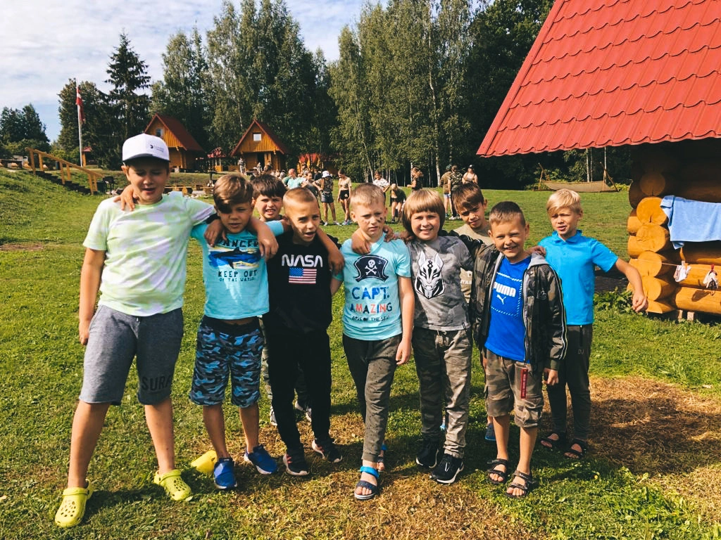 Nometnes audzinātāja apskauj bērnu uz zaļas pļavas fona bērnu nometnē.